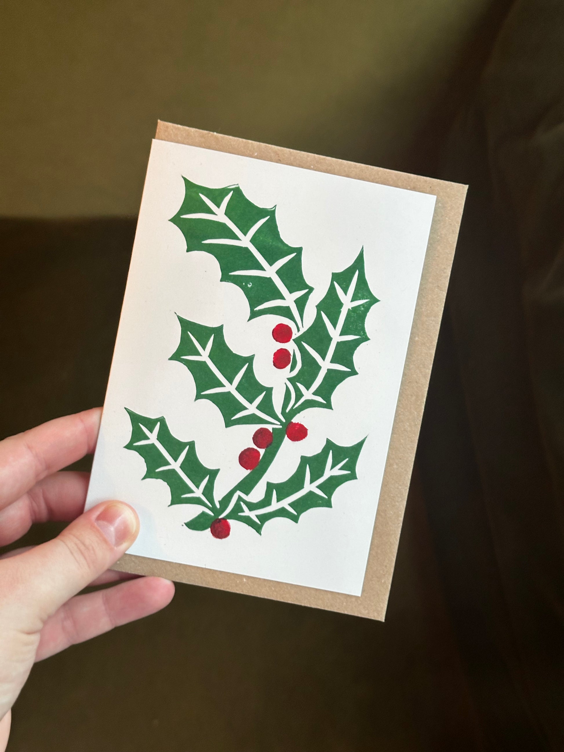 Hand holding a Christmas card with holly design on a dark background