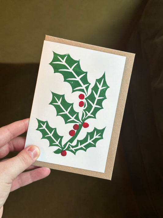 Hand holding a Christmas card with holly design on a dark background